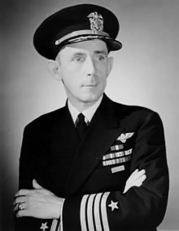 A man in a navy uniform has his arms crossed