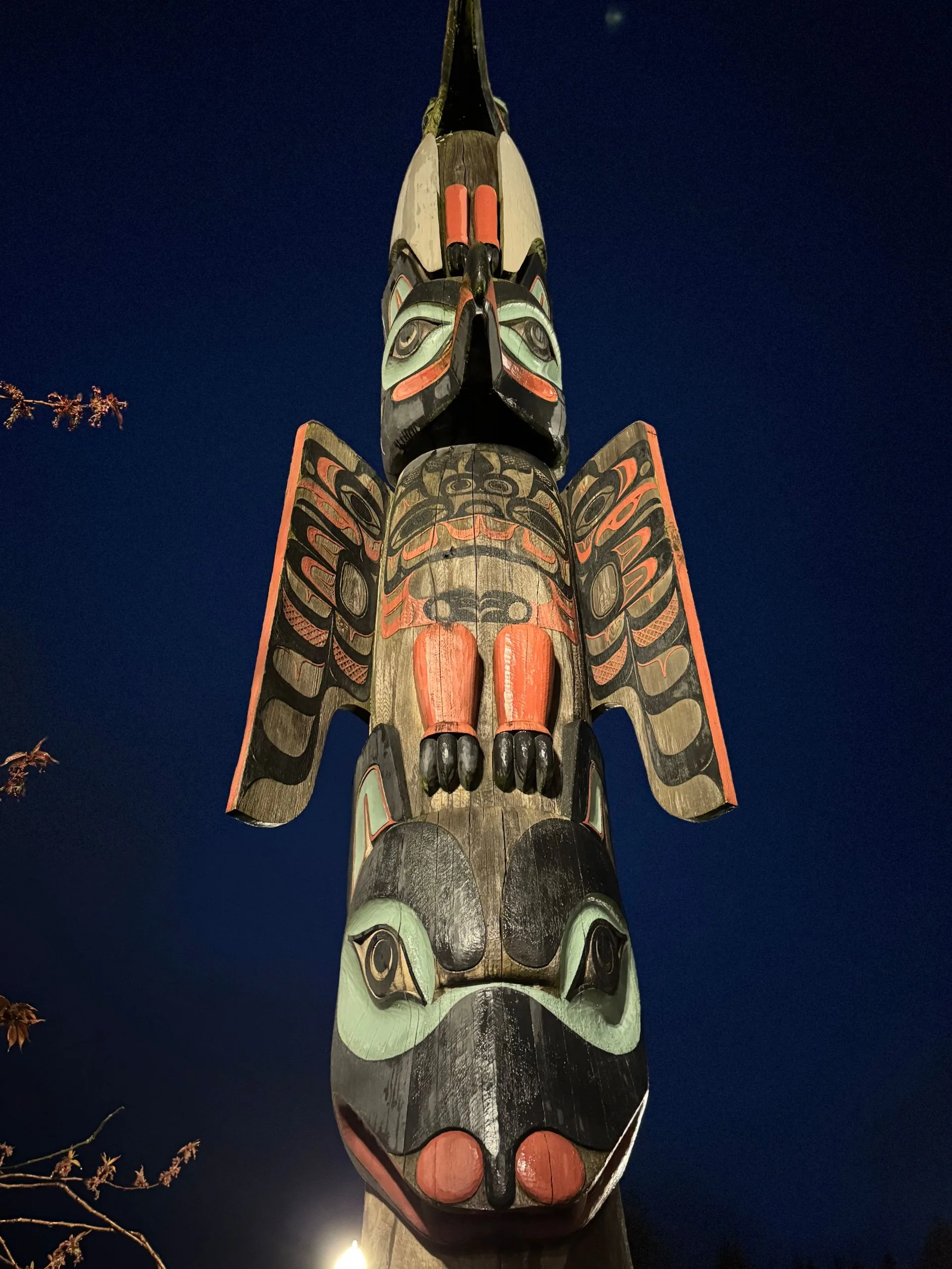 Tall, carved totem pole at night against a dark blue sky