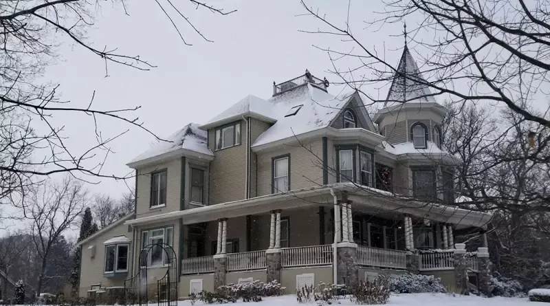 A large house with a tower on top of it is covered in snow.