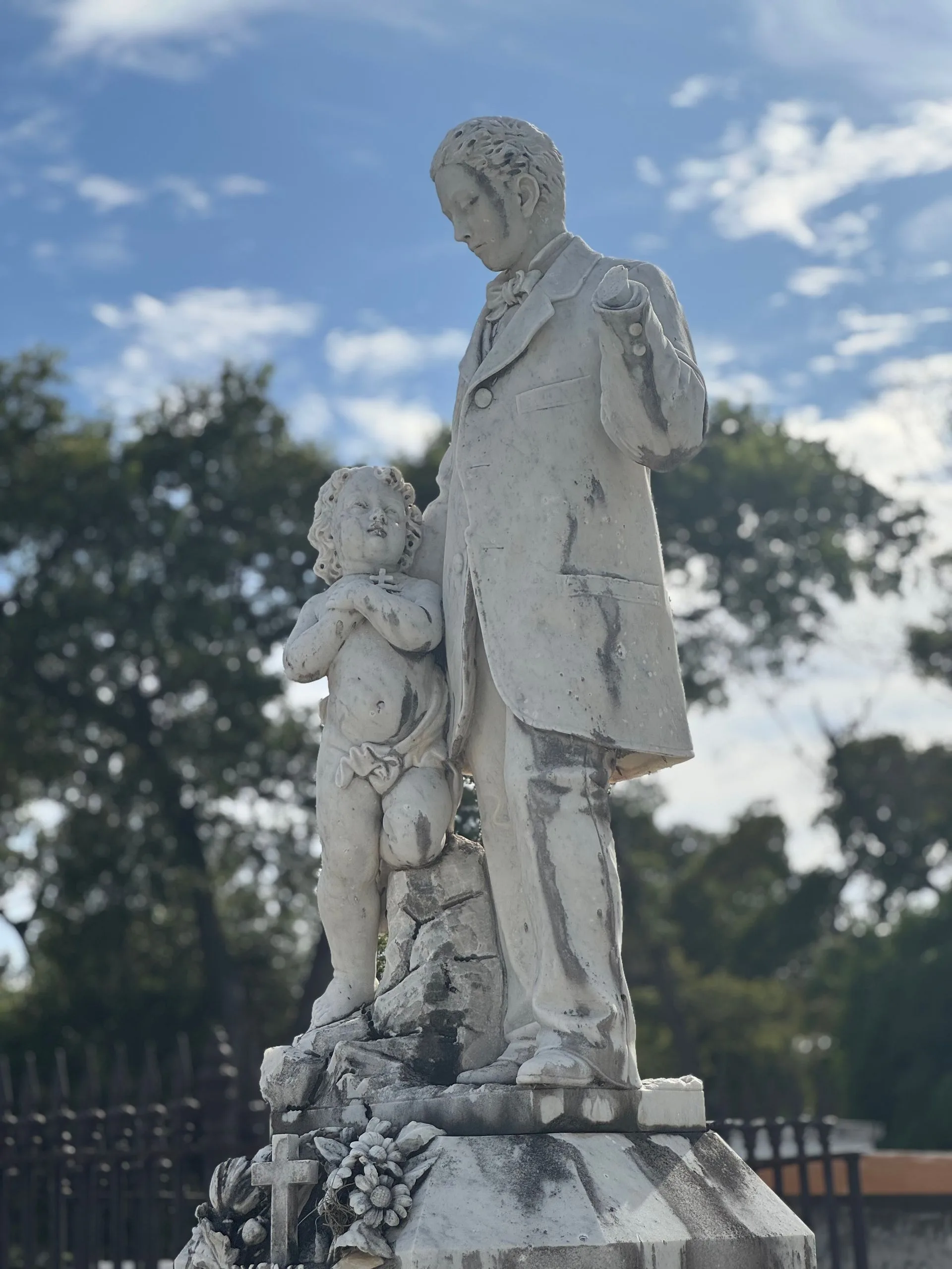 Stone statue of a man and child. Man in suit, child in short pants, both on a pedestal.