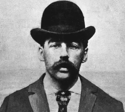 A man with a mustache and a bowler hat is wearing a suit and tie.