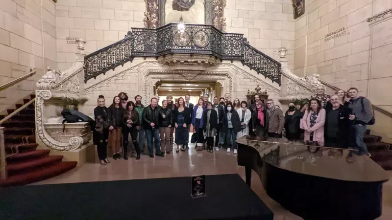 A group of people are posing for a picture in front of a piano and stairs.
