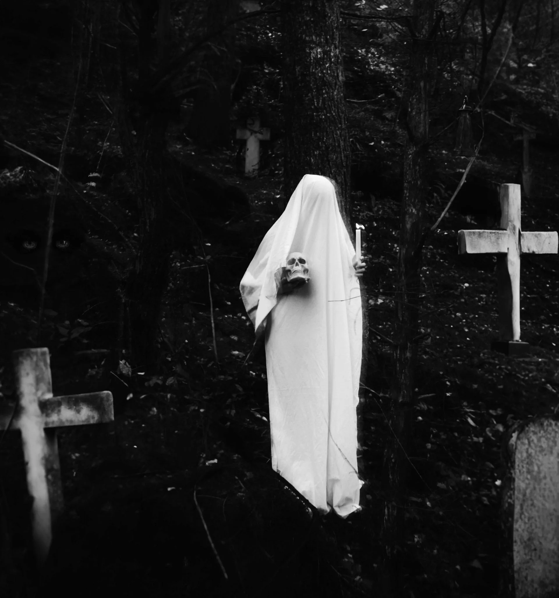 Ghostly figure in white sheet holding a skull and a candle in a dark graveyard with crosses.