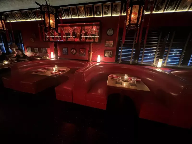 A restaurant with red booths and tables with candles on them
