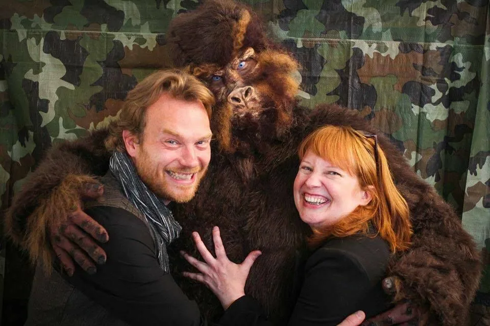 A man and a woman are posing for a picture with a stuffed gorilla.