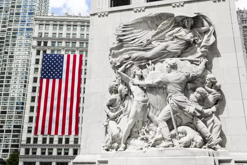 A large american flag is hanging from a statue in front of a building.
