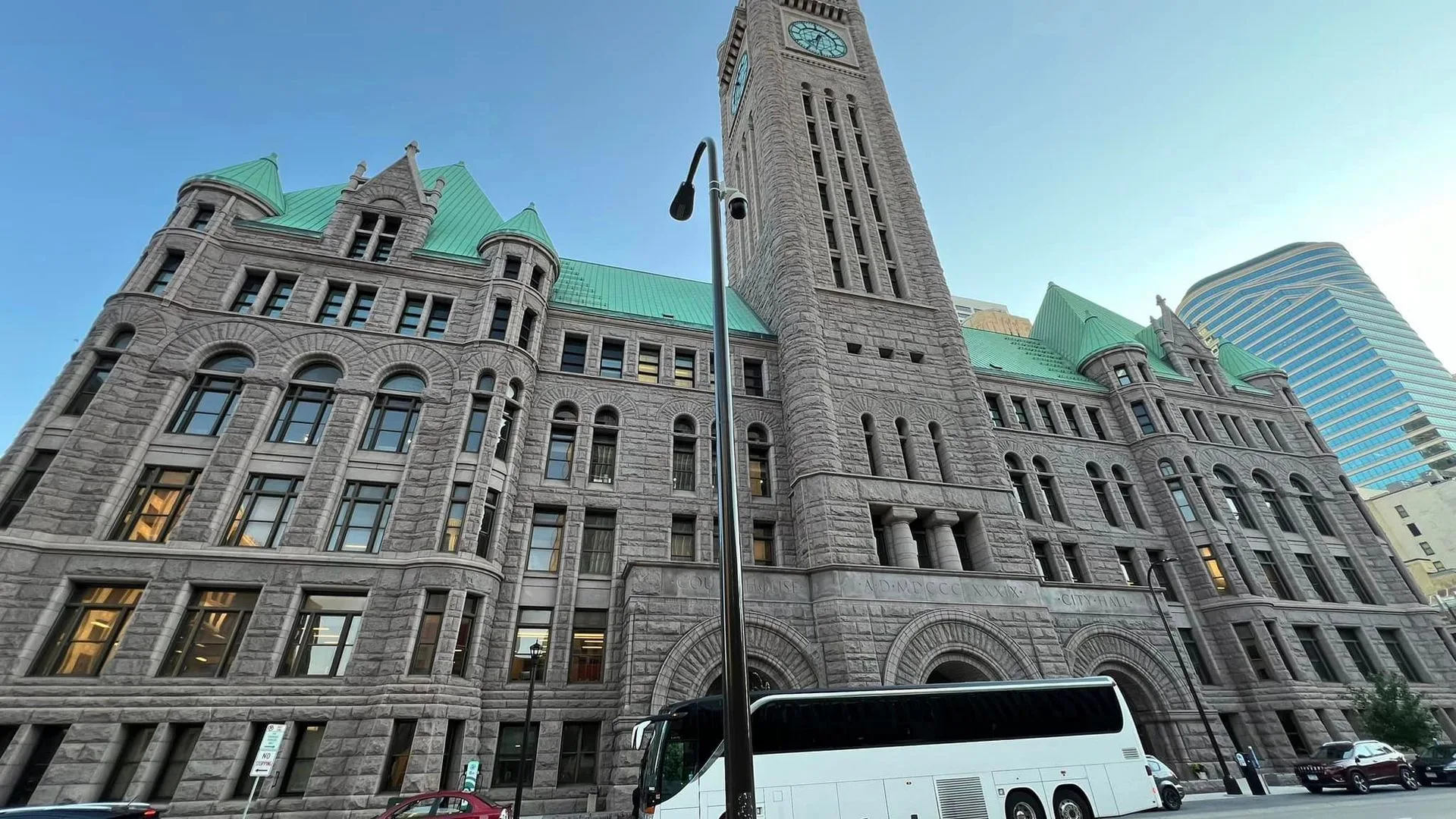 A white bus is parked in front of a large building with a clock tower
